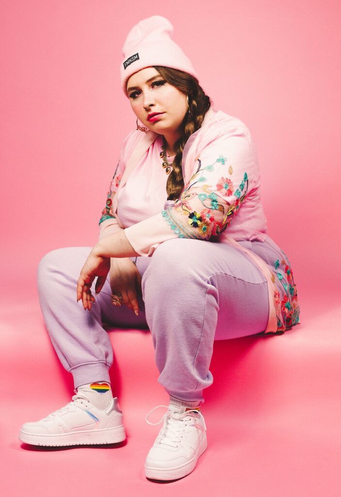 Rapperin Finna sitzt in rosa Kleidung auf einem Absatz vor rosa Hintergrund